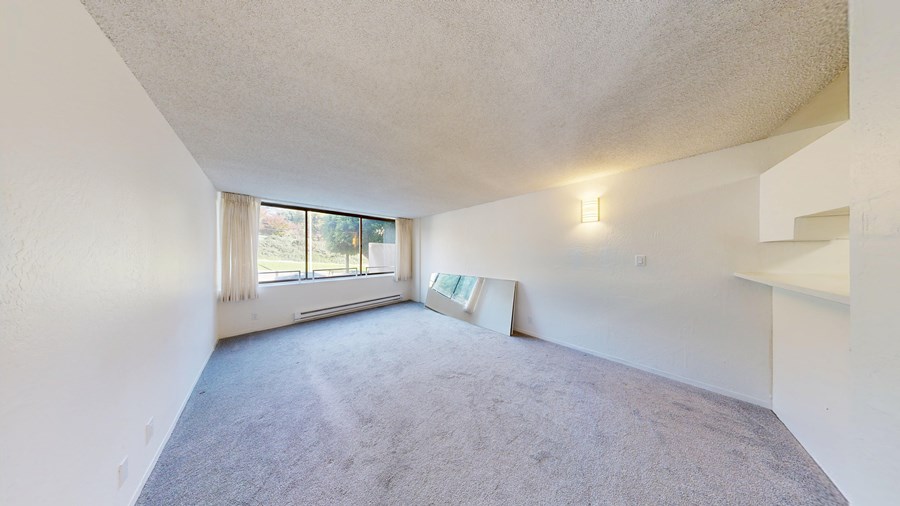 A spacious room with a carpeted floor and a window with curtains.